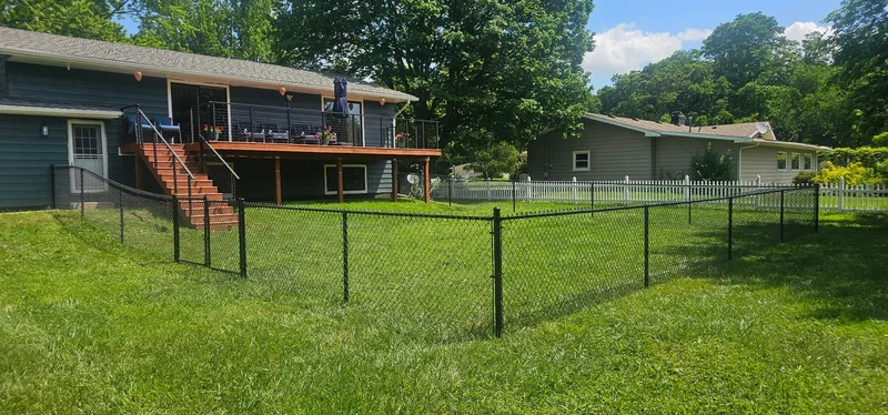 Black chain link fence enclosing residential backyard with elevated deck, Northern Indiana