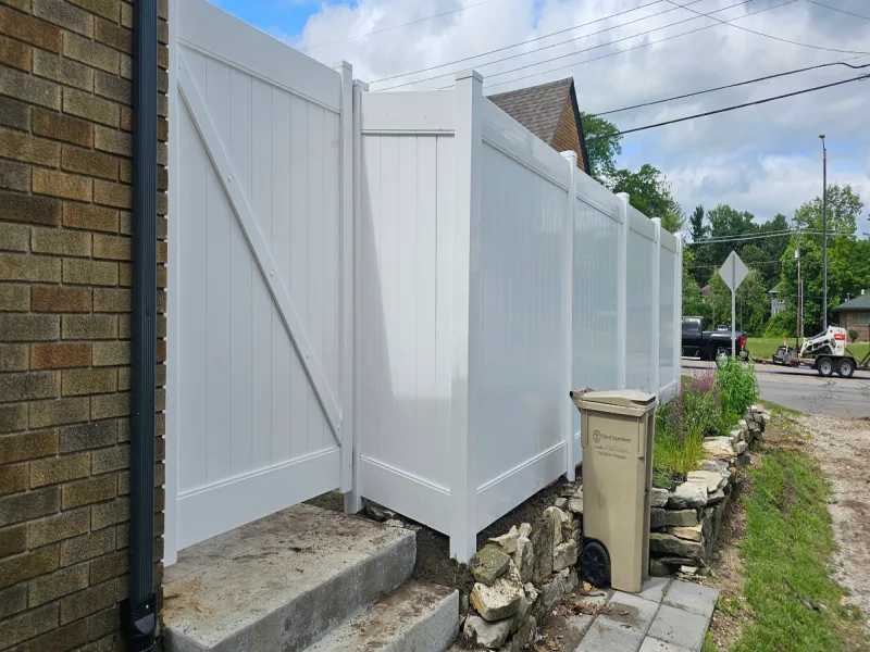 White vinyl privacy fence with double gate beside brick building, Northern Indiana installation